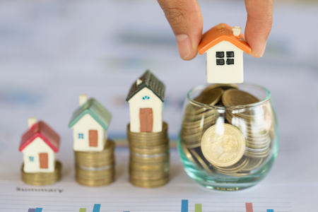 Woman hand hold a  home model put on the stack coin with growing, Savings money for buy house and loan to business investment for real estate concept. Invesment and Risk Management.の写真素材