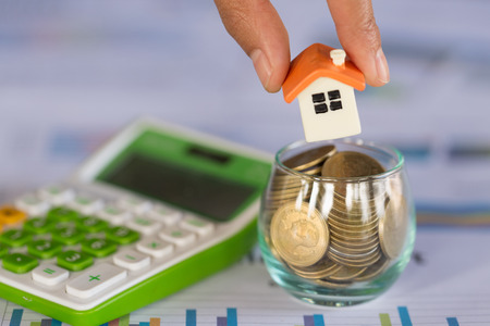 Woman hand hold a  home model put on the stack coin with growing, Savings money for buy house and loan to business investment for real estate concept. Invesment and Risk Management.の写真素材