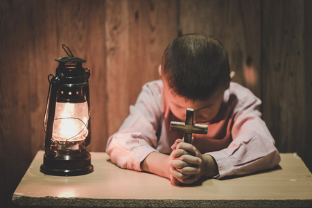Boy hands holding a holy cross  praying to God In the dark and with the lamp beside, Child Praying for God Religion.の写真素材
