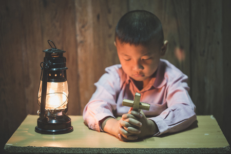 Boy hands holding a holy cross  praying to God In the dark and with the lamp beside, Child Praying for God Religion.の写真素材