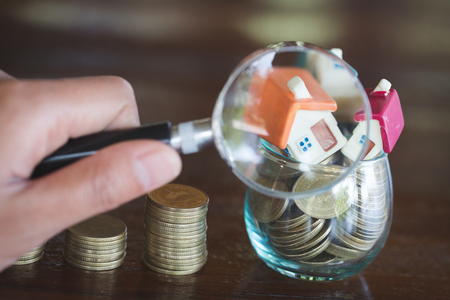 Stack coin and bar graph with grow,  Hand hold a magnifying glass searching for a new home, Loan for real estate or save money for buy a house to family in the future concept.の写真素材