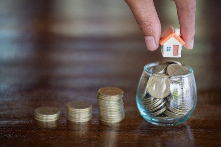Human hand putting house model on coins stack. Concept for property ladder, mortgage and real estate investmentの写真素材