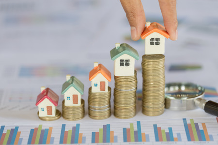 Human hand putting house model on coins stack. Concept for property ladder, mortgage and real estate investmentの写真素材