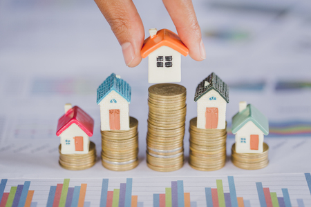 Human hand putting house model on coins stack. Concept for property ladder, mortgage and real estate investmentの写真素材