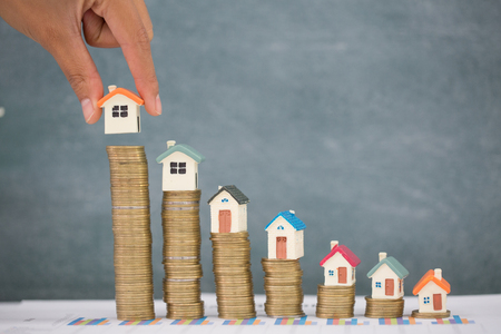 Woman hand hold a  home model put on the stack coin with growing, Savings money for buy house and loan to business investment for real estate concept. Invesment and Risk Management.の写真素材