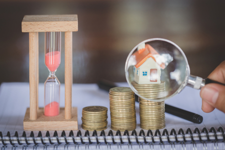 Stack coin and bar graph with grow,  Hand hold a magnifying glass searching for a new home, Loan for real estate or save money for buy a house to family in the future concept.の写真素材