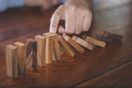 Businessman hand stopping falling wooden dominoes effect from continuous toppled or risk, strategy and successful intervention concept for business, game strategy, Invesment and Risk Management.の写真素材