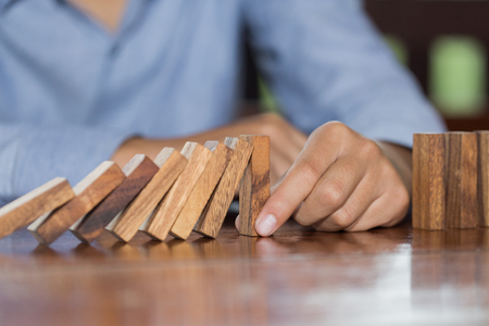 Businessman hand stopping falling wooden dominoes effect from continuous toppled or risk, strategy and successful intervention concept for business, game strategy, Invesment and Risk Management.の写真素材