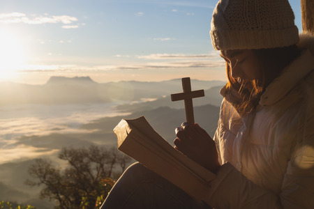 Hands holding wooden cross over open  holy bible on the mountain background with morning sunrise, spirtuality and religion,  Worship, sins and prayer.の写真素材