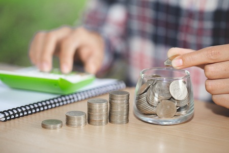 Business accounting with saving money with hand putting coins in jug glass, Businessman Writing Financial Accounting, concept financialの写真素材
