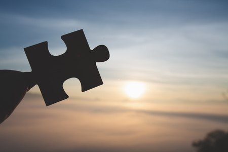 Silhouette of business woman hand holding  jigsaw puzzle piece against sunrise, Business solutions, target, success, goals and strategy conceptsの写真素材