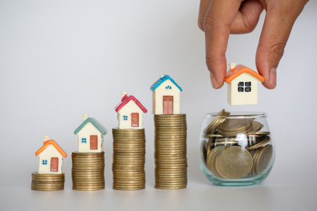 Human hand putting house model on coins stack. Concept for property ladder, mortgage and real estate investmentの写真素材