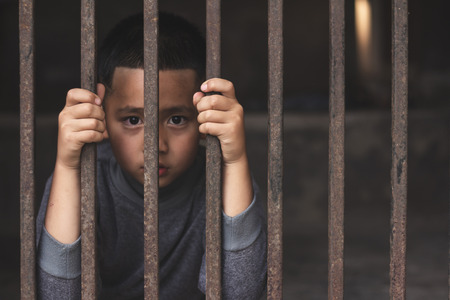 Hands of a young child clutching prison bars, victim child with locked in a cage cell, in emotional stress and pain, Children violence and abused concept.の写真素材