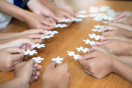 Hands of diverse people assembling jigsaw puzzle, team put pieces together searching for right...