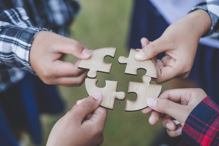 people helping in assembling puzzle, cooperation in decision making, team support in solving problems and corporate group teamwork concept, close up view of hands connecting piecesの写真素材