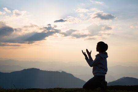 Silhouette of a woman with hands raised in the sunset concept for religion, worship, prayer and praise, Religious conceptsの写真素材