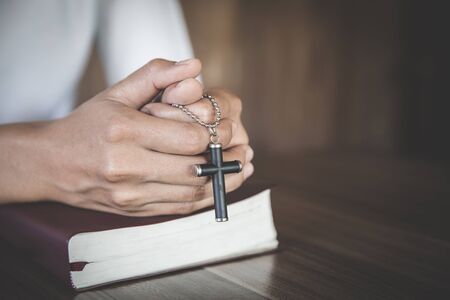 The woman holds the cross and prayes with her scriptures on the table.
