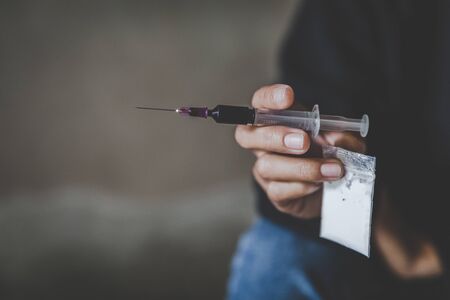 The addicted person's hand is a bag of heroin and a syringe. Anti drug concept.の写真素材