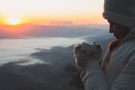 A women is praying to God on the mountain. Praying hands with faith in religion and belief in God on blessing background. Power of hope or love and devotion. の写真素材
