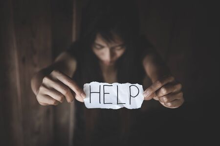 Women sitting alone with depressed expression and showing a paper with a help text. Stop violence against women.の写真素材