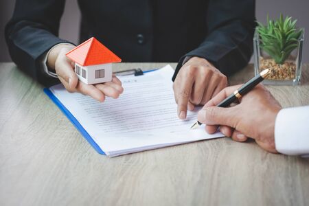 A woman signs a contract to purchase a home with a real estate agent. Model house in hand.