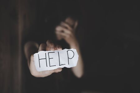 Women sitting alone with depressed expression and showing a paper with a help text. Stop violence against women.の写真素材