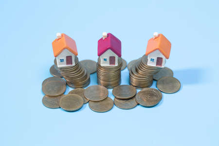 Mini house on stack of coins on a blue background. Concept of Investment property, Real estate,...