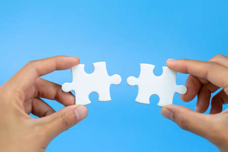 Business woman hand is trying to connect couple White jigsaw puzzle piece on a blue background. Symbol of association and connection. Concept of business strategy.の写真素材