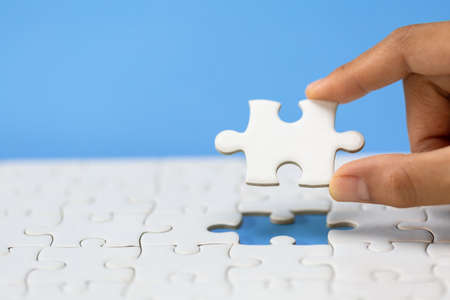 Hand put the last piece of jigsaw puzzle to complete the mission. Completing final task, missing jigsaw puzzle pieces and business concept with a puzzle piece missing.の写真素材