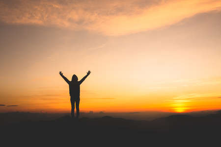 Silhouette of a woman with hands raised in the sunset concept for religion, worship, prayer and...