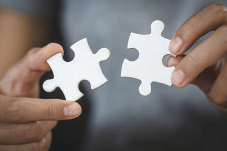 White jigsaw in the hands of humans, The correct solution. Teamwork, Solving and completing the task. Last piece of jigsaw puzzle. Assembling  jigsaw puzzle pieces.の写真素材