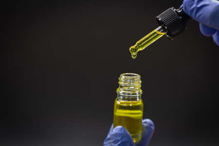 CBD hemp oil, Hand holding bottle of Cannabis oil against Marijuana plant. Herbal Treatment,...