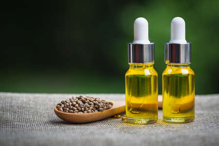 Hemp seeds and cbd hemp oil. Hemp seeds in wooden spoon and hemp essential oil in small glass bottle, medical marijuana concept.の写真素材