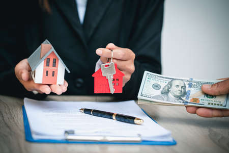 Agents are giving house keys of customer and holding dollar us. Agreement and Real estate concept.