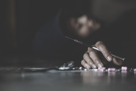 Human hand of a drug addict and a syringe with narcotic syringe lying on the floor. World Anti-drug Day. - Imageの写真素材
