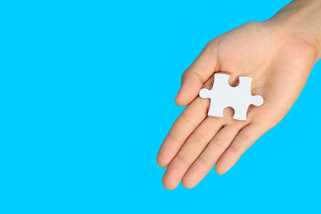 white jigsaw puzzle pieces in  hand on blue background, The last piece of jigsaw puzzle, Copy space.