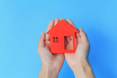 Red house in the hands of a businessman. Blue background. Real estate concept. Mortgage to address. Home care. Home for the family.の写真素材
