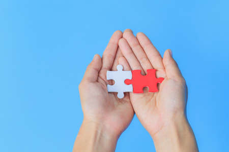 White and red jigsaw puzzles. Placed on hand to hand together. Blue background. The concept of cooperation. Joint investment. Cooperation to be successful. Team work.の写真素材