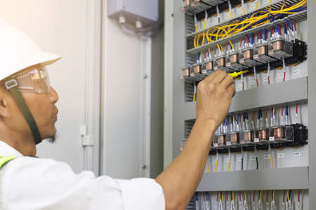 A male electrician works in a control panel with electrical connections connecting devices with a complex working concept tool.の写真素材