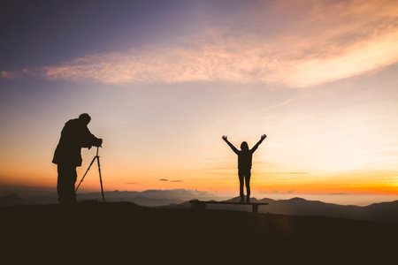 Silhouette of photographer taking photo with model on mountain at sunset, professional wedding photographyの写真素材