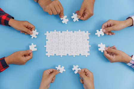 Group of business people assemble jigsaw puzzles on blue background,  teamwork, help and support in...