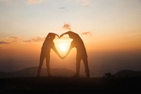 A woman and a man make a heart at sunrise on the mountain. god is love concept heart shape mountain travel manifestation of love love and feelingsの写真素材