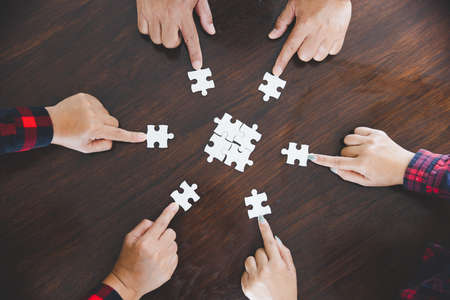 people helping in assembling puzzle, cooperation in decision making, team support in solving problems and corporate group teamwork concept, close up view of hands connecting piecesの写真素材
