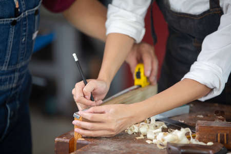A carpenter works with equipment on a wooden table in a carpentry shop.