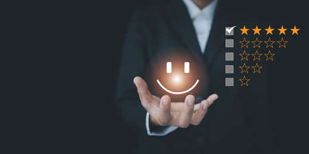 Customer Service Assessment Concept. Businessman holding smiley face showing virtual emoticon, survey, poll or questionnaire for user experience or customer satisfaction research.の写真素材