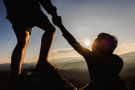 Silhouette of hiker helping each other hike up a mountain at sunset. People helping and, team work concept.の写真素材