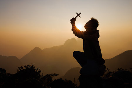 Silhouette of a man with a crucifix in his hands praying to God. while the sun is rising Praise the religion. Supreme Faith in the God of Success. Adventure, Travel, Religious Faith.の写真素材