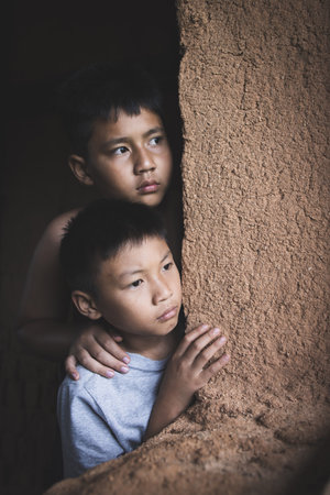 Closeuptwo poor children peeking out of a dilapidated house, Concept of assistance to the poor, human rights, violence against children.の写真素材