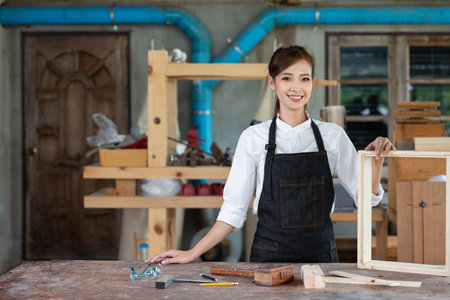 Young woman is training to be a carpenter in workshop. Carpenter working with equipment on wooden table. woman works in a carpentry shop.の写真素材