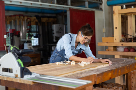 Young woman is training to be a carpenter in workshop. Carpenter working with equipment on wooden table. woman works in a carpentry shop.の写真素材